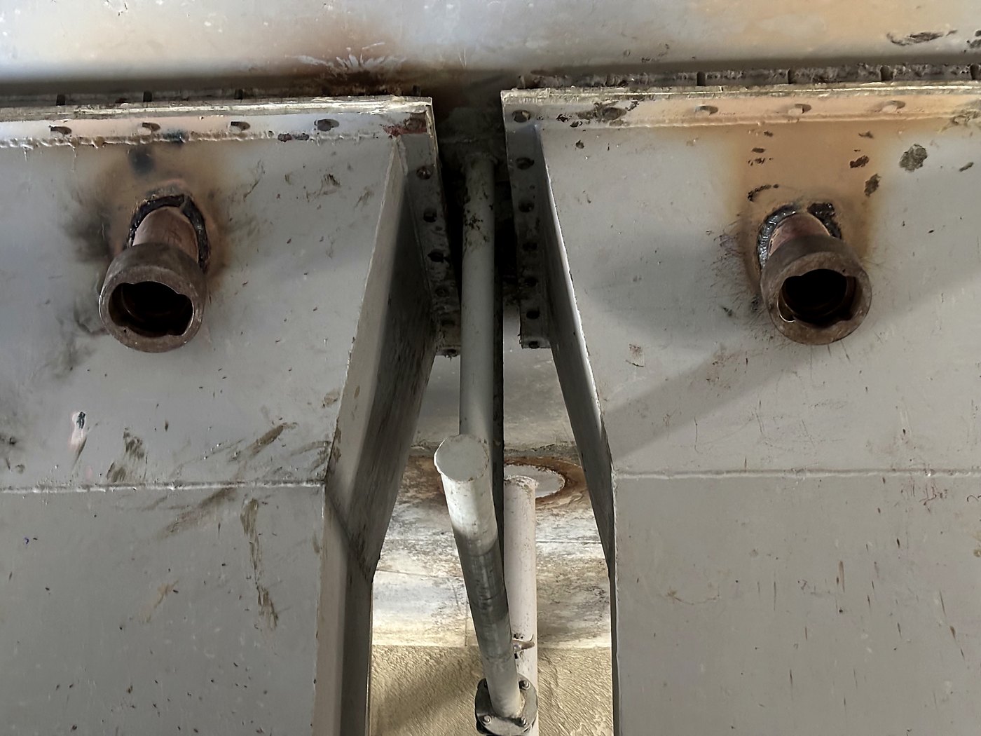 Two Cardox sockets welded through the wall of a silo discharge chute, seen from below, with the weld beads and heat discolouration visible around each socket body