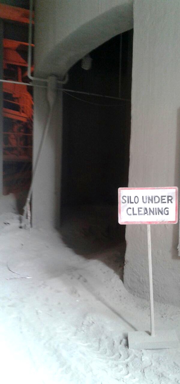 A silo doorway during a cleaning job, signed SILO UNDER CLEANING, with cement dust across the floor